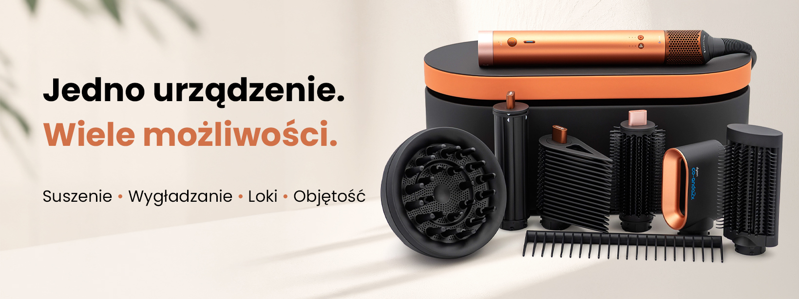 Reklamowy baner Dyson przedstawia miedziano-czarny zestaw do stylizacji na jasnym tle, z napisami Jedno urzadzenie. Wiele możliwości. Główny korpus leży na czarnej stacji z pomarańczowym akcentem, otoczony różnymi czarnymi końcówkami i szczotkami.