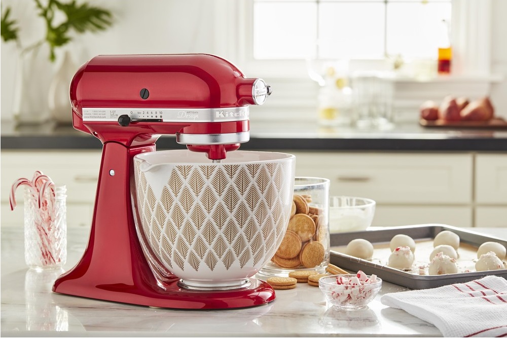 Czerwony robot kuchenny KitchenAid Artisan 5KSM175PSECA z misą w liściasty wzór, na blacie kuchennym z ciasteczkami i słodyczami do pieczenia.