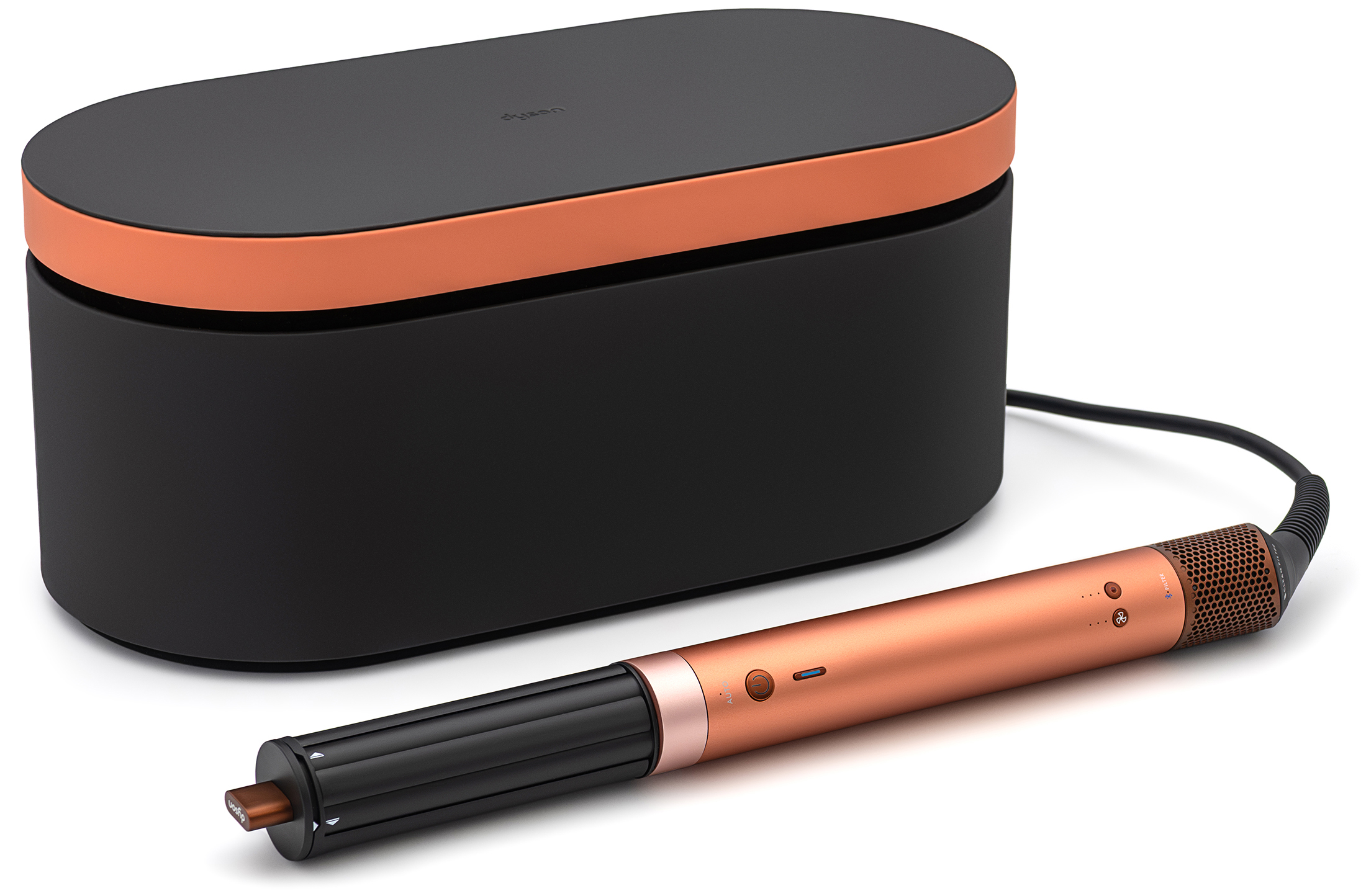 Lokówko-suszarka Dyson Airwrap Co-anda2x Curly+Coily w odcieniu bursztynowego jedwabiu, ustawiona pod kątem obok czarnego etui z miedzianą pokrywą na białym tle. Urządzenie posiada miedziany korpus z panelem sterowania, na którym umieszczono przycisk zasilania oraz wskaźniki funkcyjne. Do korpusu przymocowana jest czarna, podłużna końcówka do stylizacji, a z tyłu obudowy widoczna jest teksturowana sekcja filtra oraz czarny przewód zasilający.