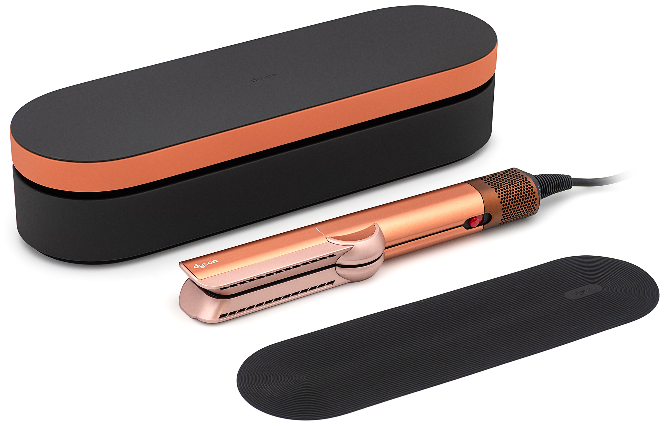 Aeroprostownica Dyson Airstrait w odcieniu miedziano-różowym Amber Silk prezentowana jest w dwóch ujęciach na białym tle, obok czarnego etui oraz silikonowej podkładki. Po lewej stronie widoczne jest urządzenie w pozycji otwartej z panelem sterowania wyposażonym w przyciski oraz czarnym wnętrzem ramion. Po prawej stronie prostownica pokazana jest w pozycji zamkniętej. W górnej części znajduje się czarne etui z miedzianym akcentem, a poniżej leży czarna podkładka.