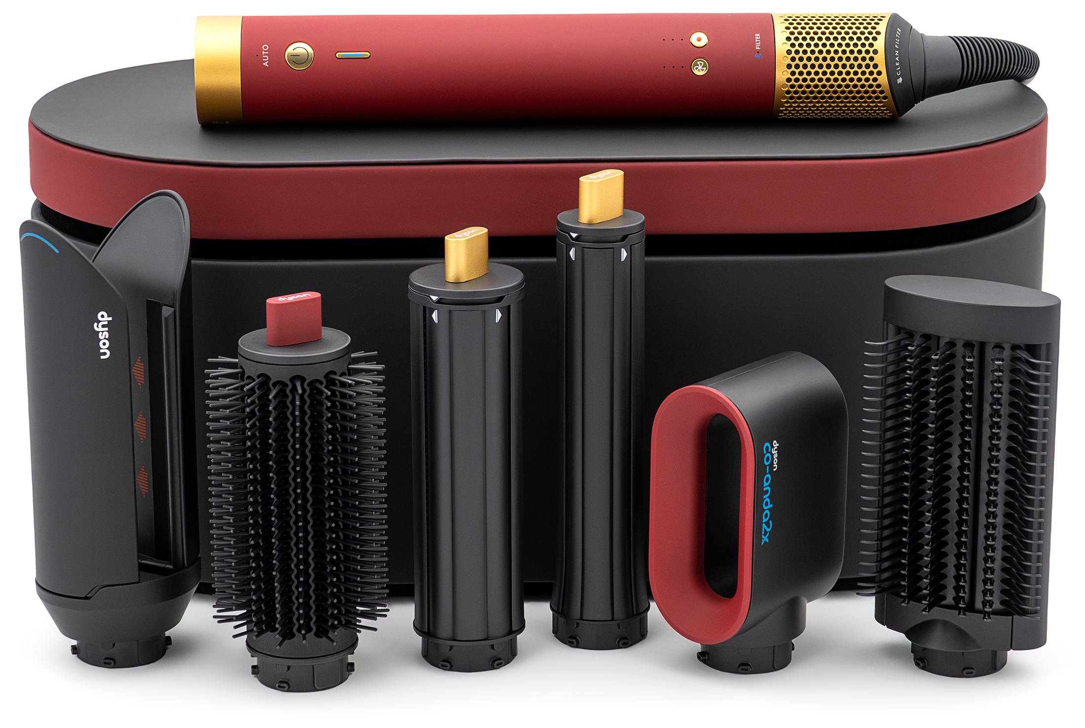 Zestaw Dyson Airwrap Multistyler w kolorze aksamitnej czerwieni ze złotymi akcentami. Główny moduł urządzenia spoczywa na etui, a przed nim w rzędzie ustawiono sześć czarnych wymiennych końcówek do kompleksowej stylizacji włosów.