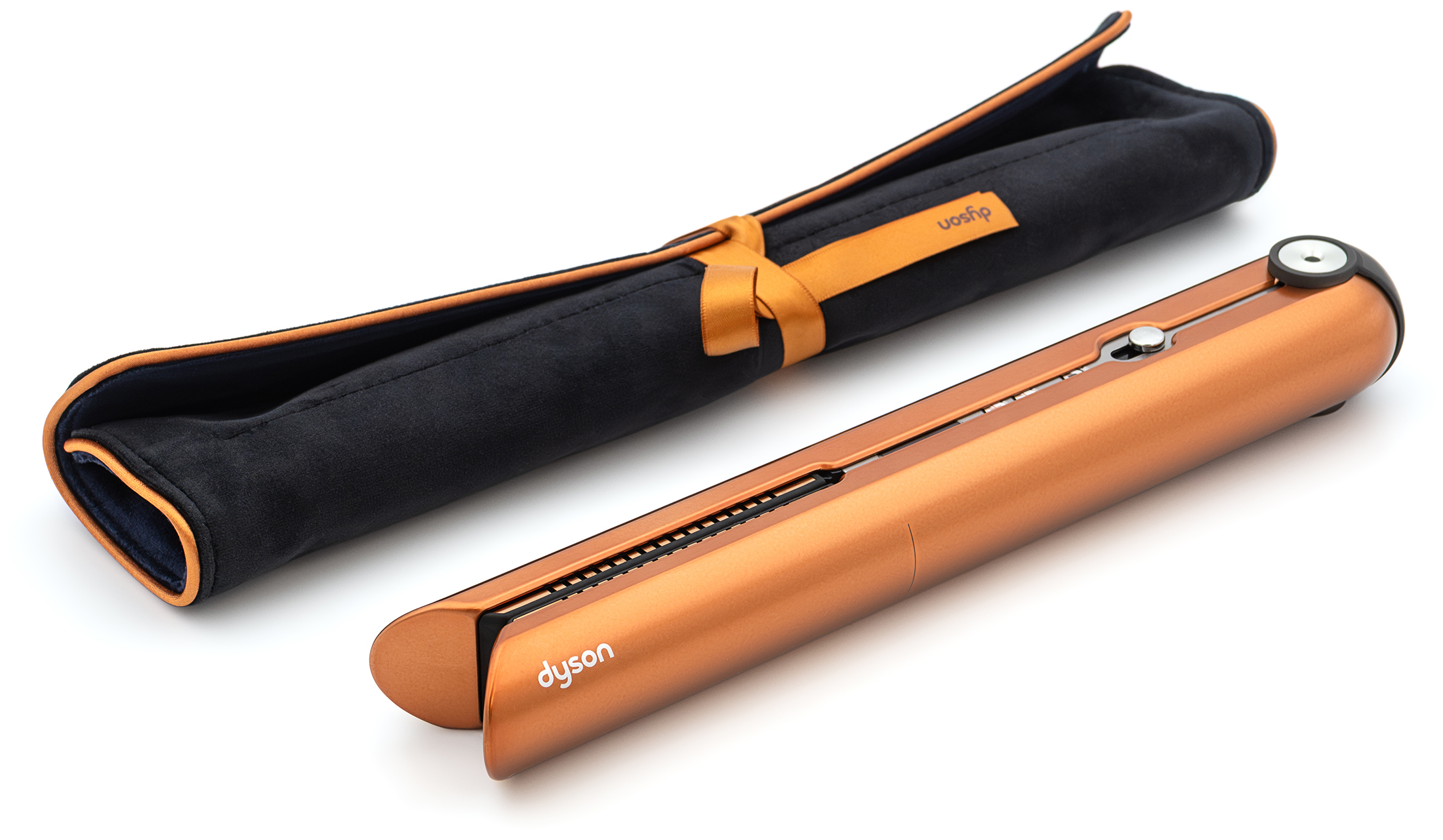 Miedziana prostownica bezprzewodowa Dyson Corrale leży obok czarnego, aksamitnego etui podróżnego na jasnym tle. Urządzenie jest złożone, prezentując elegancki design i srebrne detale wykończenia. Etui posiada estetyczne miedziane obszycie oraz ozdobne wiązanie wstążką.