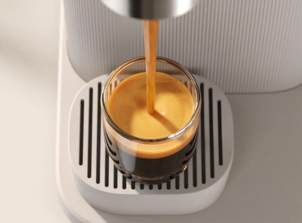 Zbliżenie od góry na nalewanie espresso do szklanki w ekspresie Philips Baristina BAR300/03. Strumień kawy tworzy gęstą piankę crema na powierzchni naparu. Szklanka stoi na jasnej tacy ociekowej ze szczelinami.
