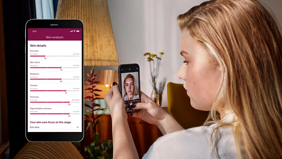 Kobieta patrzy na smartfon z aplikacją Philips Lumea 9900 BRI977/00 SenseIQ, która wyświetla wyniki analizy skóry.