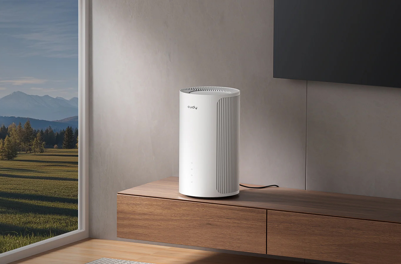 Router Cudy P2 5G stoi na drewnianej szafce w jasnym, nowoczesnym salonie obok telewizora. Przez duże okno obok urządzenia roztacza się widok na góry i las. Router jest biały, ma cylindryczny kształt i pionowe żebrowania na bocznych ściankach.