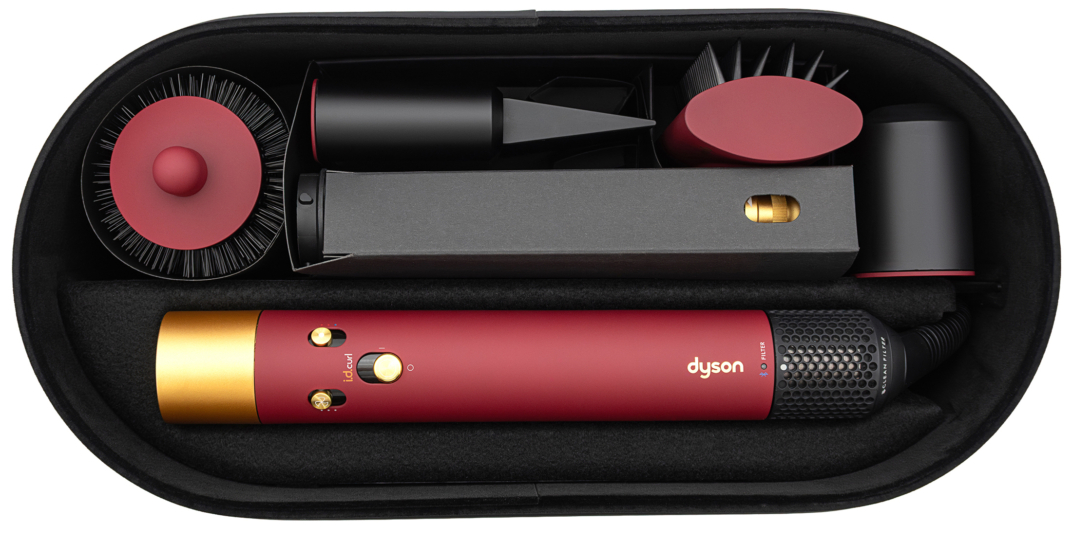 Zestaw stylizacyjny Dyson Airwrap i.d. Curly+Coily w otwartym czarnym etui, widok z góry. Wewnątrz znajduje się czerwone urządzenie główne ze złotymi detalami oraz komplet wymiennych końcówek w kolorach czerni i czerwieni na białym tle.