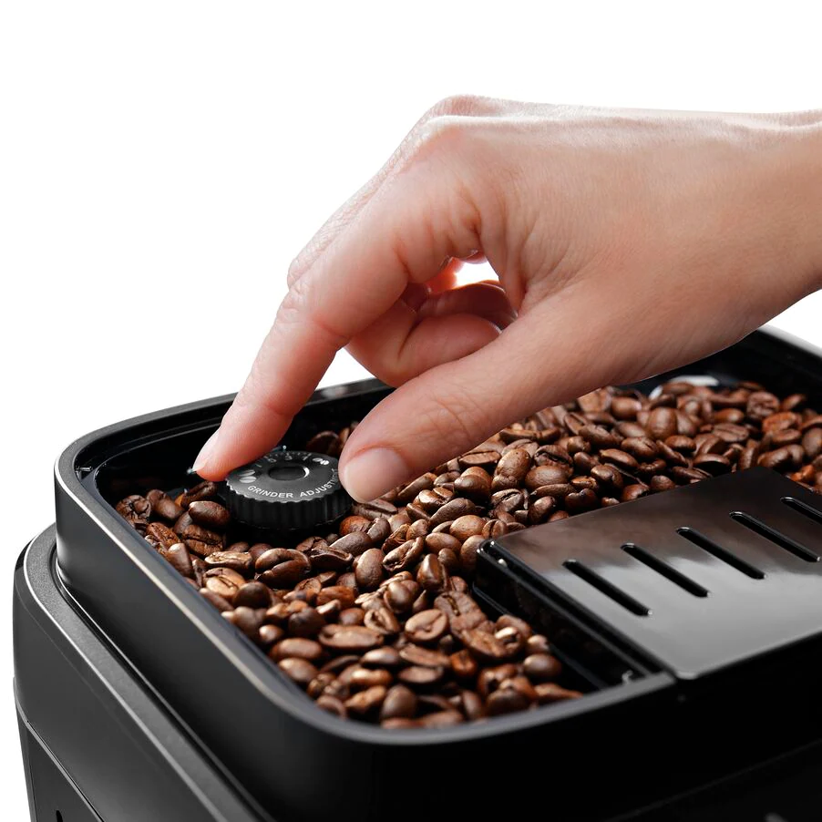 Zbliżenie na pojemnik ekspresu DeLonghi z ziarnami kawy, gdzie dłoń reguluje pokrętłem stopień mielenia.