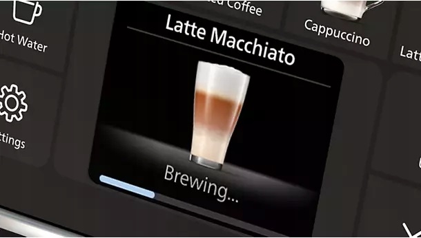 Zbliżenie na wyświetlacz ekspresu Philips LatteGo Series 5500. Ekran pokazuje proces przygotowywania kawy Latte Macchiato z napisem Brewing... i paskiem postępu. Widoczne są również ikony menu ustawień i gorącej wody na czarnym panelu sterowania.