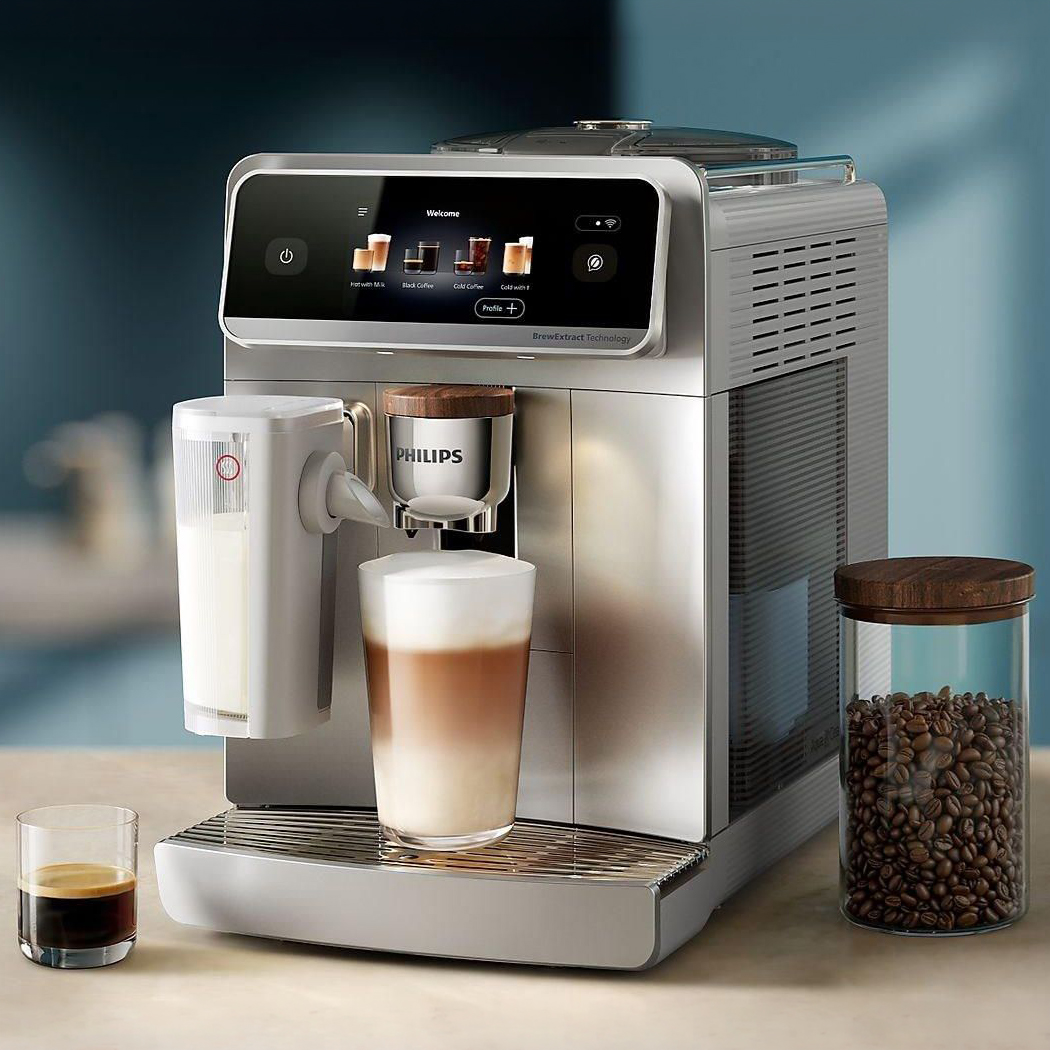 Ekspres Philips LatteGo Pro EP8757/20 w kolorze srebrnym z przygotowaną kawą latte i espresso na blacie. Obok stoi szklany pojemnik z ziarnami kawy. Urządzenie prezentuje nowoczesny design z dużym wyświetlaczem i eleganckimi drewnianymi akcentami.