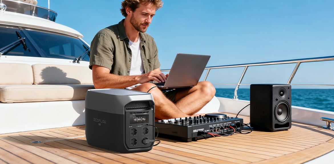 Mężczyzna pracuje na laptopie na pokładzie jachtu, zasilając komputer, konsolę DJ i głośnik przenośną stacją zasilania EcoFlow Delta 3 Max. Urządzenie w ciemnoszarej obudowie stoi obok niego, a jego wyświetlacz wskazuje 100 procent naładowania. W tle widać morze.