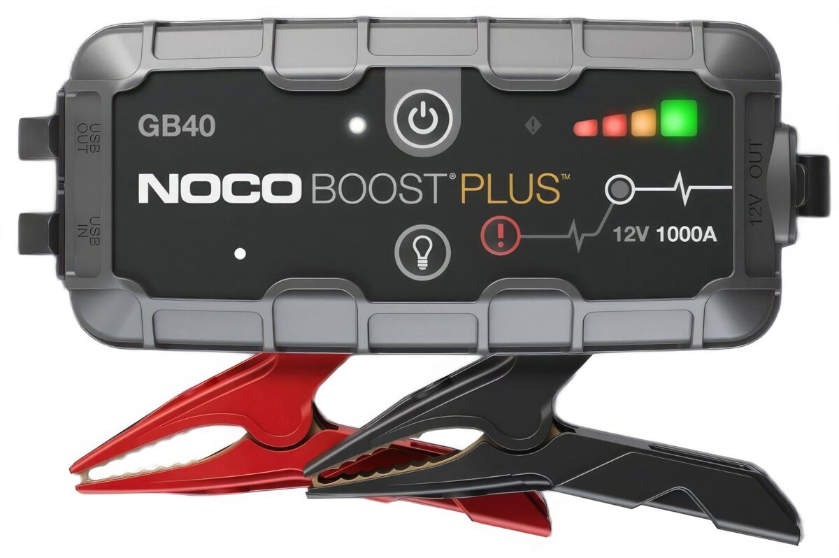 Urządzenie rozruchowe NOCO Boost Plus GB40 z czerwonym i czarnym zaciskiem, widok od frontu na białym tle. Na panelu widoczne jest logo marki, wskaźnik naładowania LED, ikona latarki oraz przycisk ostrzegawczy.