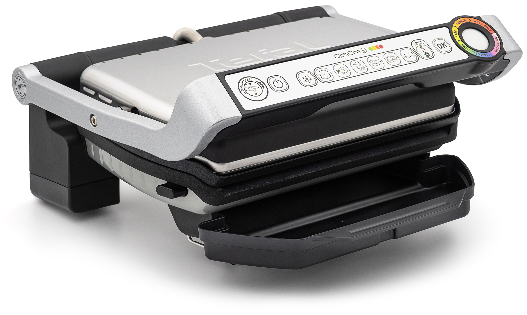 Zamknięty grill elektryczny Tefal GC716D12 OptiGrill+ w srebrno-czarnej obudowie, zaprezentowany pod kątem na białym tle. Urządzenie posiada wysuniętą dolną tacę ociekową z czarnego plastiku. Na rączce grilla wyraźnie wyeksponowano panel sterowania z ikonami programów oraz okrągłym, kolorowym wskaźnikiem stopnia wysmażenia potraw.