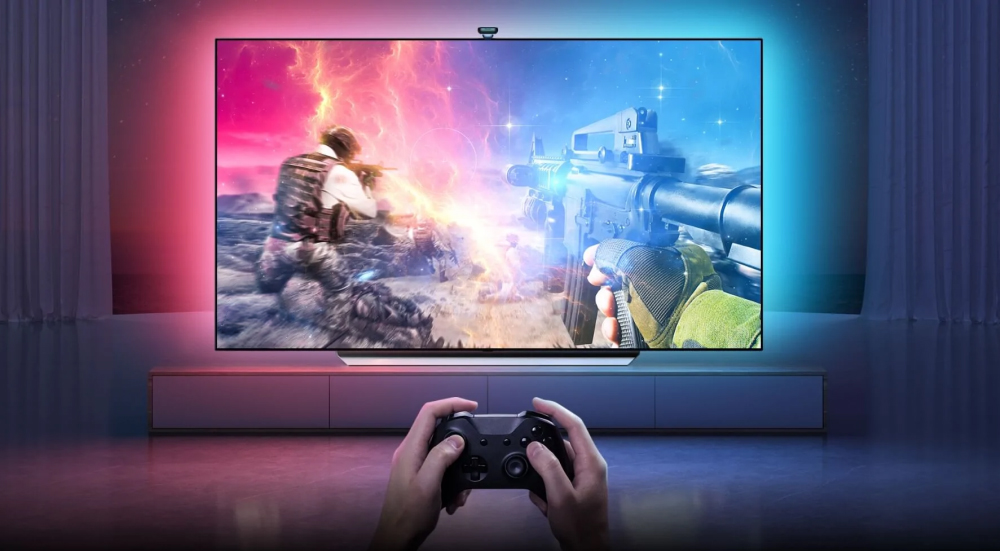 Telewizor z podświetleniem Govee TV Backlight T2 podczas grania w grę wideo. Efektowna synchronizacja światła z obrazem tworzy kolorową poświatę na ścianie, dopasowaną do akcji na ekranie. Na pierwszym planie widoczne ręce z padem do konsoli.