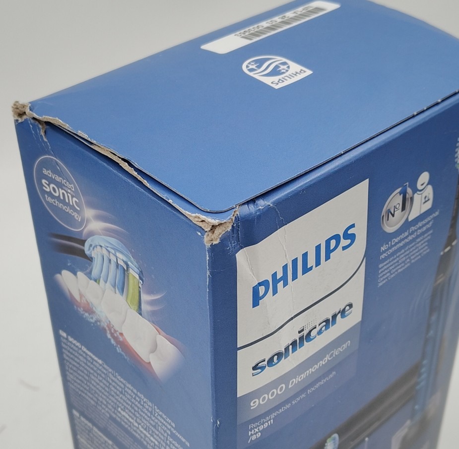 Pudełko szczoteczki Philips Sonicare 9000 DiamondClean HX9911/89 z wyraźnie uszkodzonym, rozdartym górnym rogiem i zgnieceniami na krawędziach. Widok z perspektywy bocznej ukazuje logotypy marki oraz grafikę produktową na niebieskim tle.