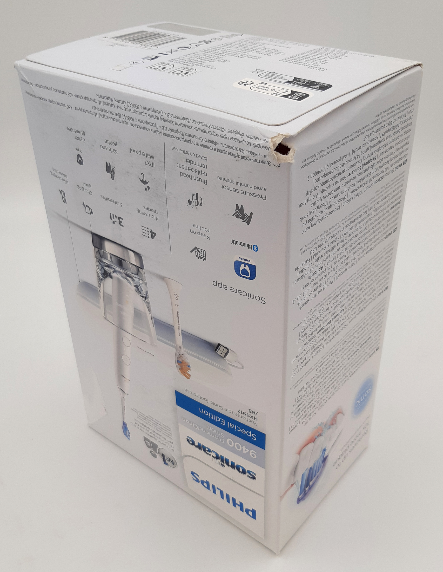 Zdjęcie prezentuje uszkodzone pudełko szczoteczki Philips Sonicare DiamondClean Smart. Na górnej krawędzi kartonu widoczne jest głębokie wgniecenie oraz naderwanie materiału. Całość ujęta z perspektywy ukazującej stan zewnętrzny opakowania na neutralnym tle.