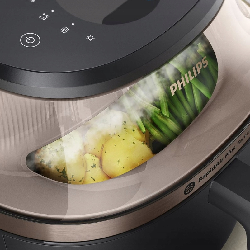 Zbliżenie na podświetlone okienko frytkownicy Philips Airfryer NA547/07 z zaparowaną szybką. Wewnątrz widać ugotowane ziemniaki i zieloną fasolkę szparagową. U góry widoczny jest fragment panelu dotykowego.