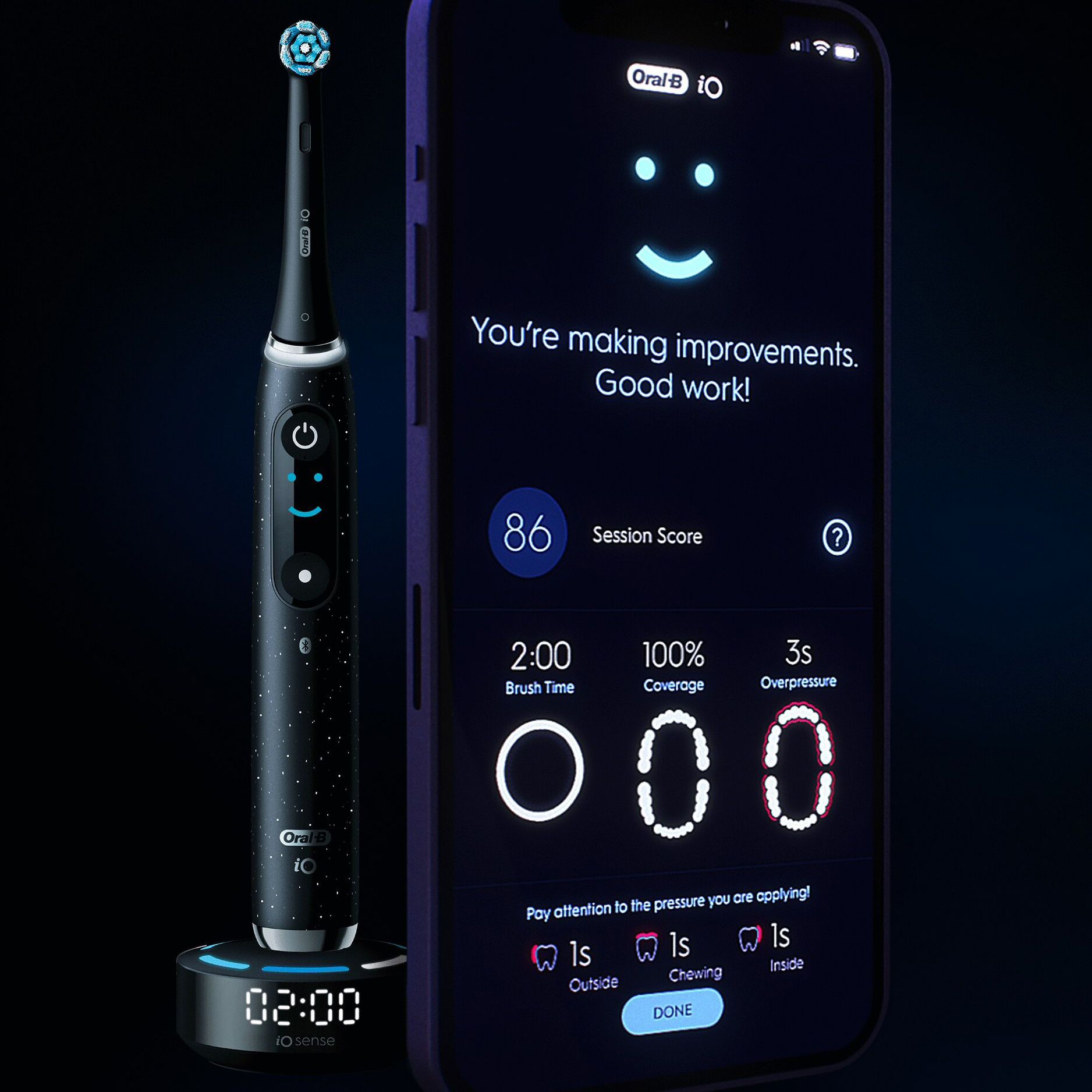 Czarna szczoteczka magnetyczna Oral-B iO Series 10 na stacji ładującej z widocznym czasem 02:00. Obok ekran smartfona wyświetla podsumowanie mycia zębów w aplikacji Oral-B iO, pokazujące wynik 86 i pełne pokrycie powierzchni zębów.
