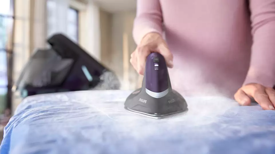 Kobieta prasuje niebieską koszulę żelazkiem Philips PerfectCare 8000 PSG8160/30, z którego unosi się dużo pary.