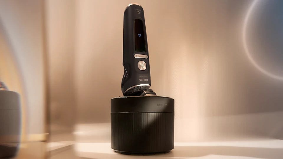 Czarna golarka elektryczna Philips S9000 Prestige SP9840/32 umieszczona w czarnej stacji ładującej. Golarka ma podświetlany wyświetlacz i metaliczne akcenty. Całość stoi na jasnym blacie w stonowanym, kremowym wnętrzu z rozmazanym tłem.