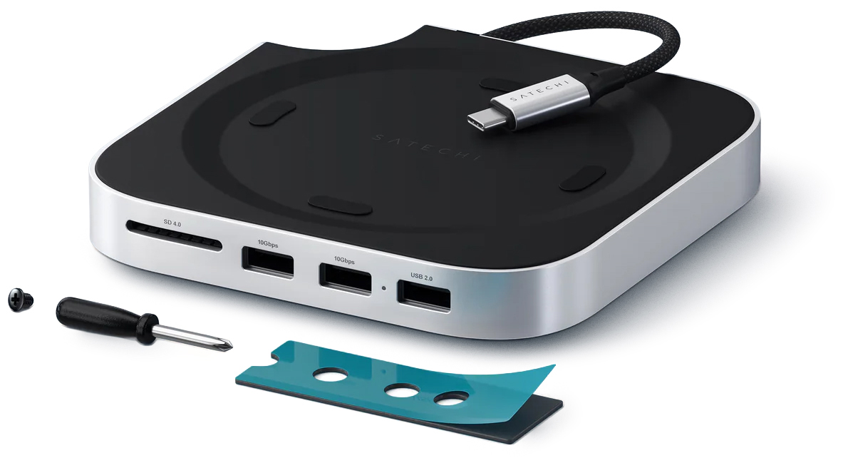 Srebrna stacja Satechi Stand and Hub dla Mac Mini M4 z dołączonymi akcesoriami montażowymi. Obok urządzenia widoczny jest mały śrubokręt, śrubka oraz element wykończeniowy. Widok prezentuje przedni panel z portami USB-C i czytnikiem kart oraz kabel przyłączeniowy.