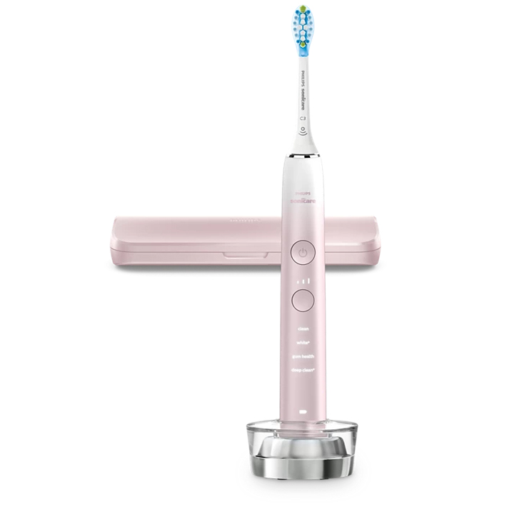 Jasnoróżowa szczoteczka soniczna Philips Sonicare 9000 DiamondClean umieszczona w szklanej ładowarce. W zestawie znajduje się również różowe etui podróżne. Szczoteczka posiada białą końcówkę oraz podświetlany panel z wyborem programów czyszczenia.