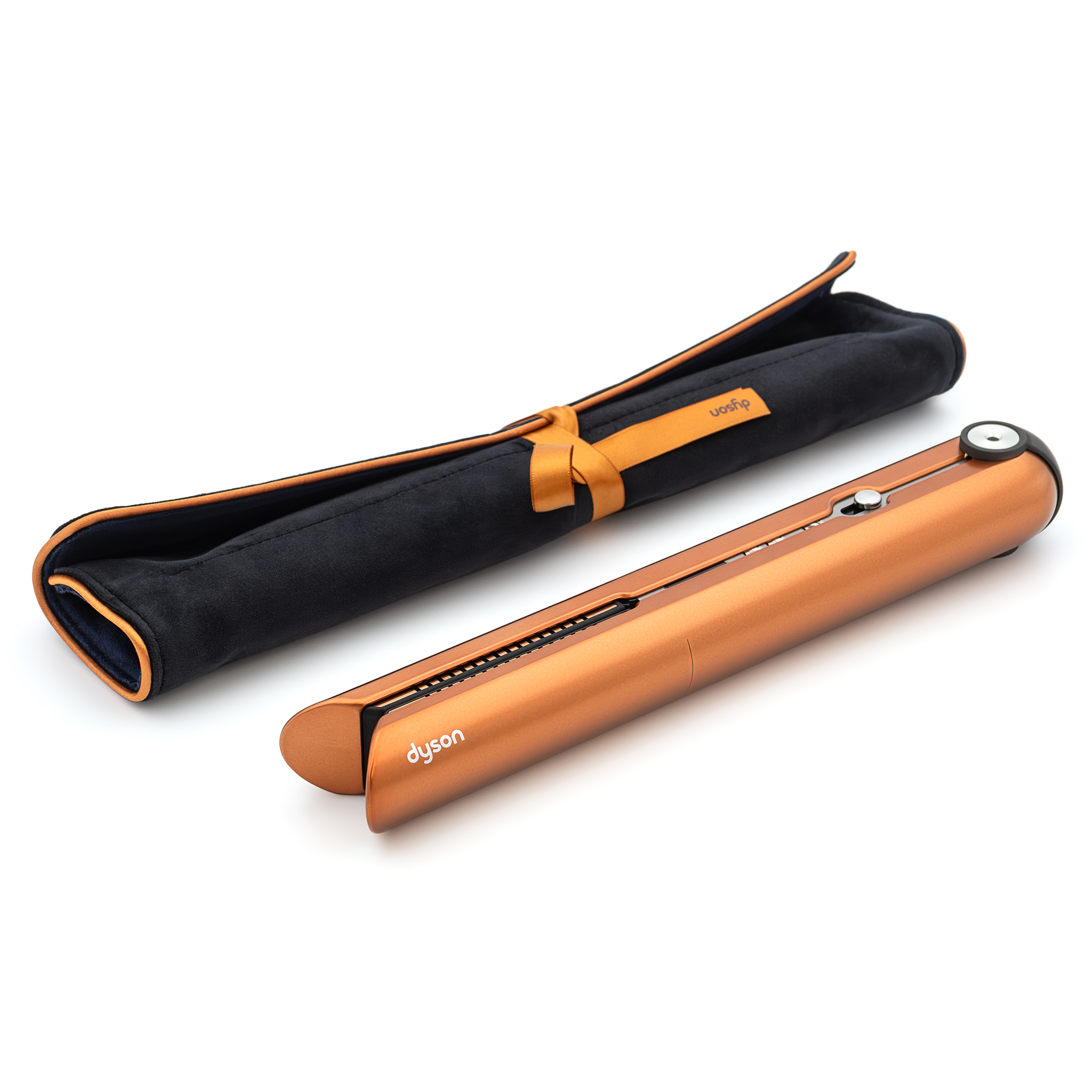 Miedziana prostownica bezprzewodowa Dyson Corrale leży obok czarnego, aksamitnego etui podróżnego na jasnym tle. Urządzenie jest złożone, prezentując elegancki design i srebrne detale wykończenia. Etui posiada estetyczne miedziane obszycie oraz ozdobne wiązanie wstążką.